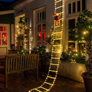 Santa Claus climbing ladder with warm LED lights on house wall.